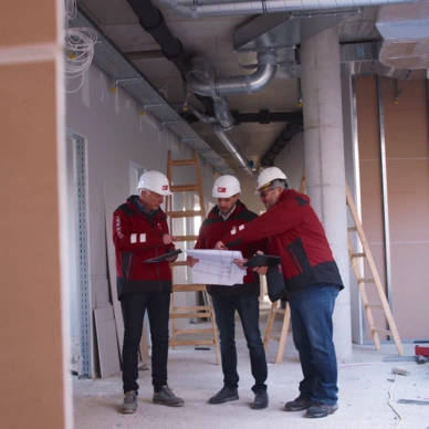 Drei Mitarbeiter auf der Baustelle, die sich einen Plan anschauen.